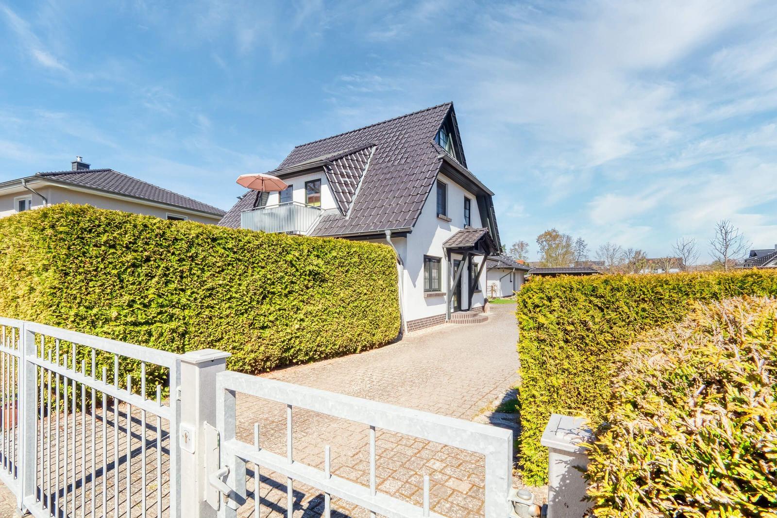 Haus mit Balkon, gepflegtem Garten und Zufahrt. Hinterhof mit Hecke und Tor.