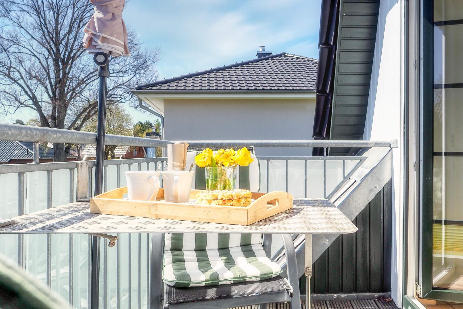 Balkon mit Tisch, Stuhl und Frühstückstablett mit Blumen und Tassen.