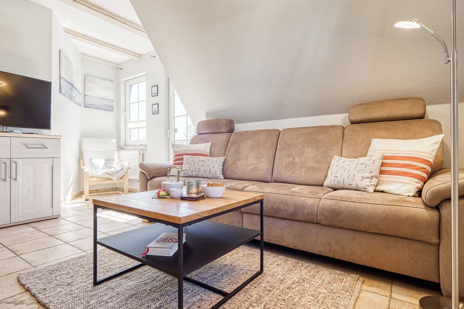 Ein Wohnzimmer mit braunem Sofa, Holz-Tisch und Fernseher an der Wand.