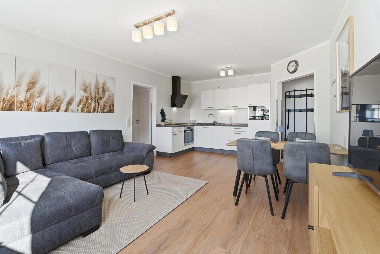 Wohn- und Küchenbereich mit grauem Sofa, Essplatz und moderner Küchenzeile.