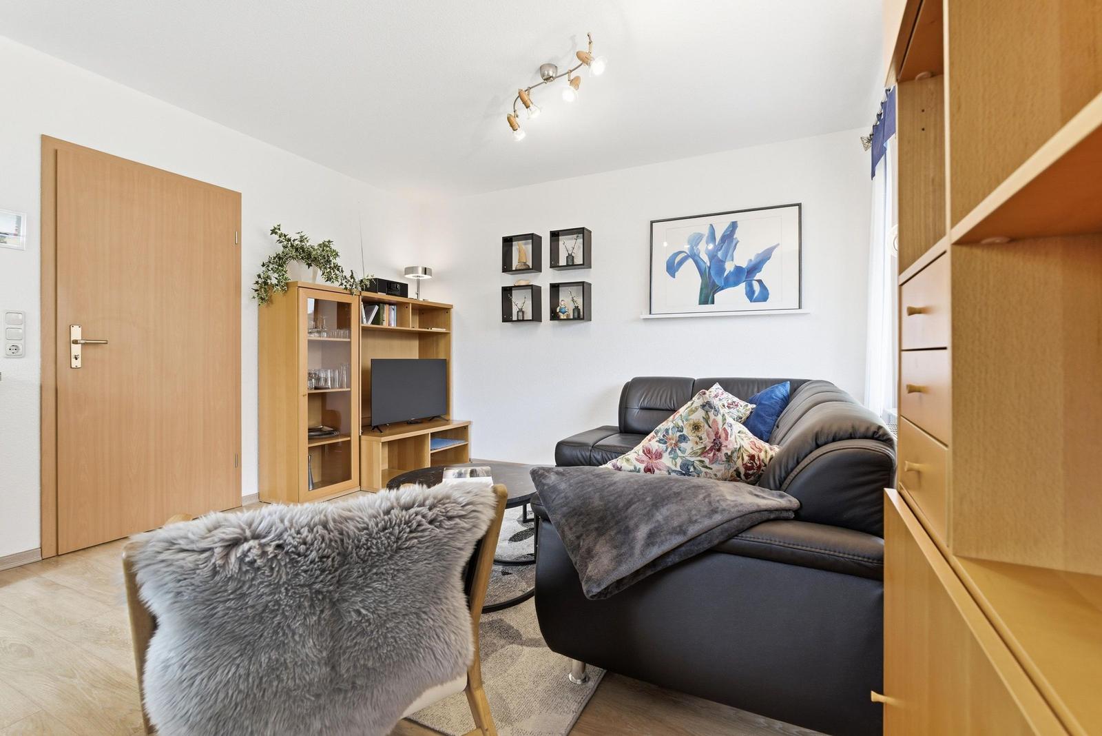 Wohnzimmer mit Sofa, Fernseher und Holzmöbeln. Wandbild und Pflanzen sorgen für Stil.