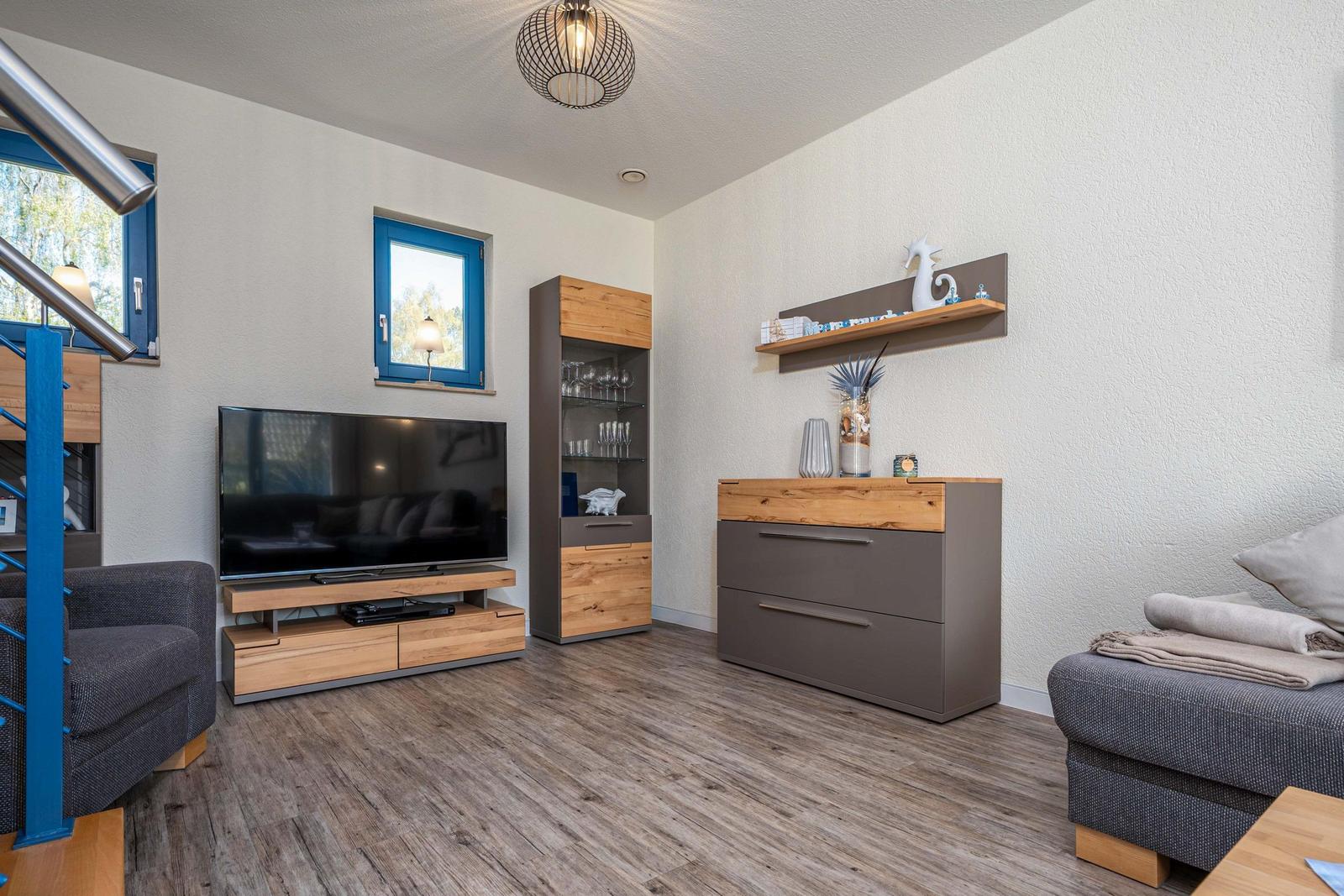 Wohnzimmer mit TV, Schränken und blauen Fenstern.