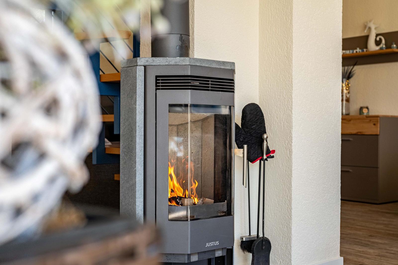 Holzofen mit brennendem Feuer, daneben stehen Ofenhandschuhe und -utensilien.