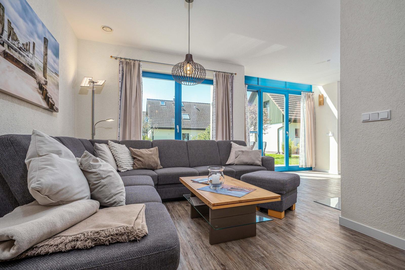 Ein Wohnzimmer mit grauem Sofa, Holztisch und blauen Fenstern.