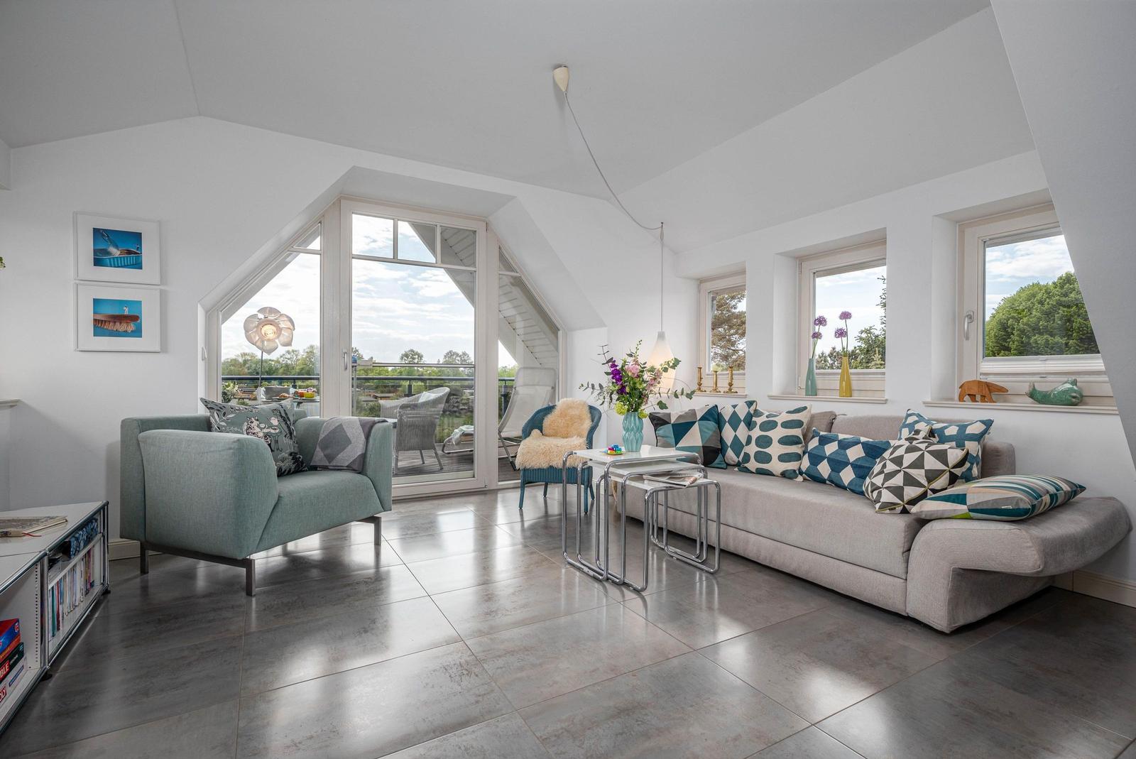 Wohnraum mit Sofa, Sessel und großem Fenster zum Balkon.