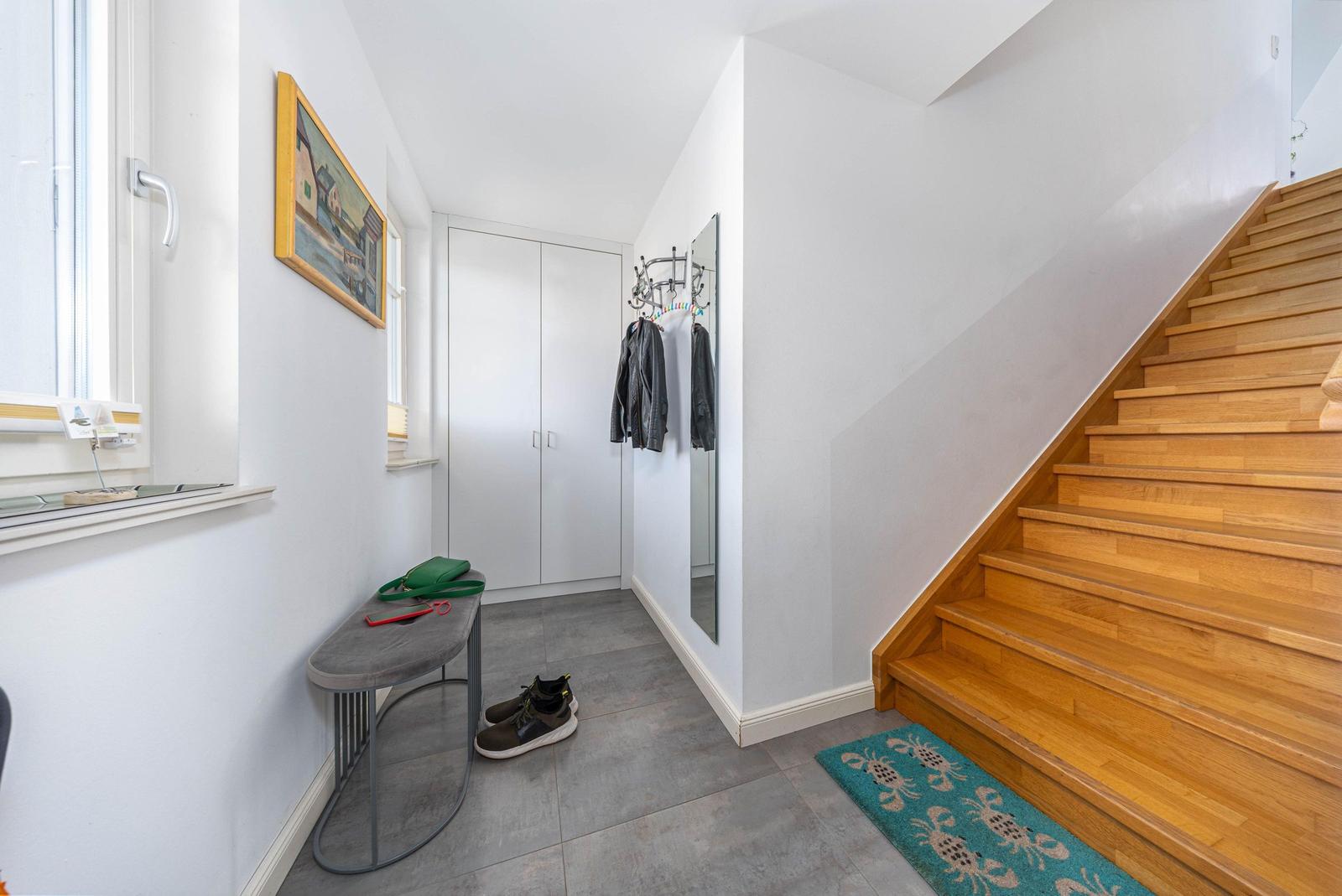 Eingangsbereich mit Treppe, Garderobe und Fenster. Auf dem Boden liegt ein Teppich mit Krabbenmuster.