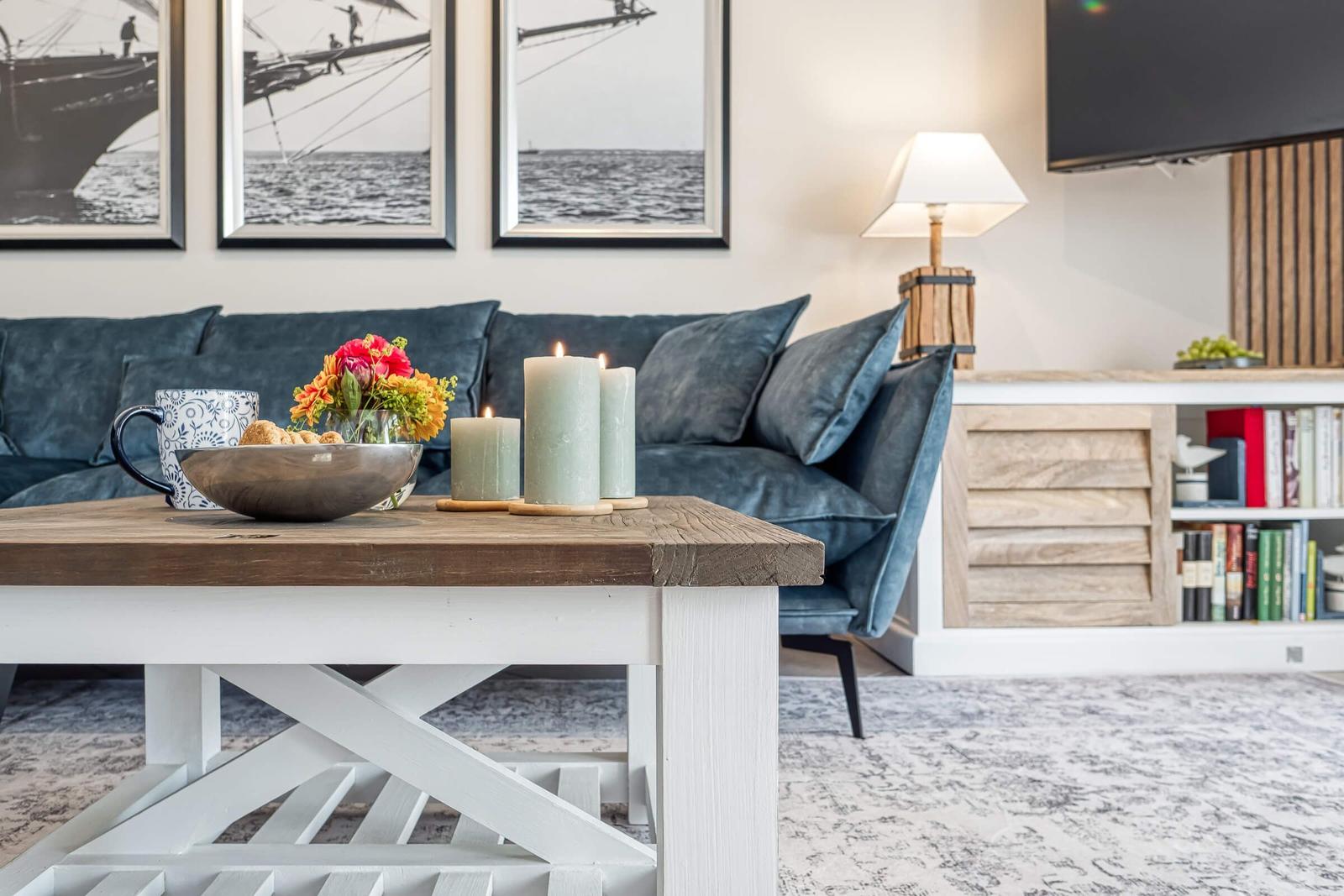 Ein Wohnzimmer mit blauem Sofa, Holztisch und Wandbildern über dem Sofa.
