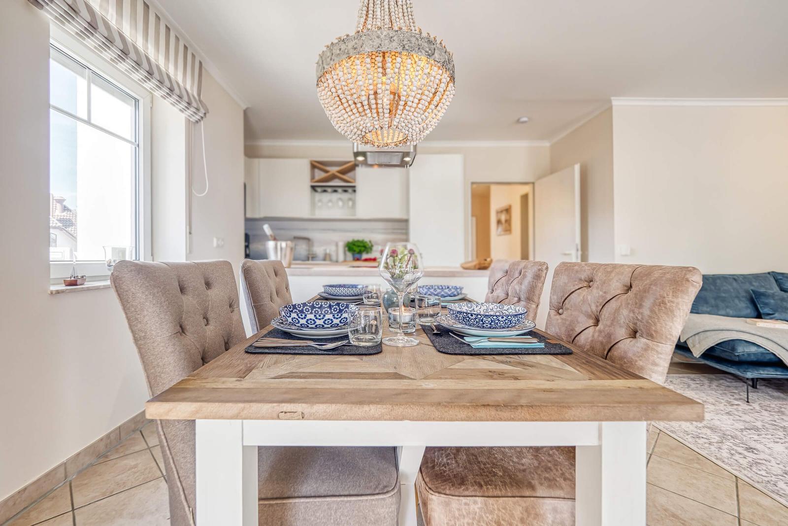 Esszimmer mit Holztisch, Stühlen und Kronleuchter. Küche und Wohnzimmer im Hintergrund.