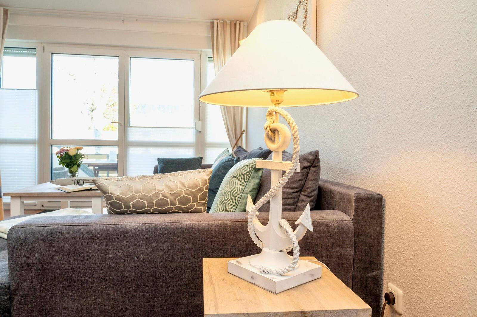 Lamp on coffee table with anchor decor. Sofa with cushions near window.