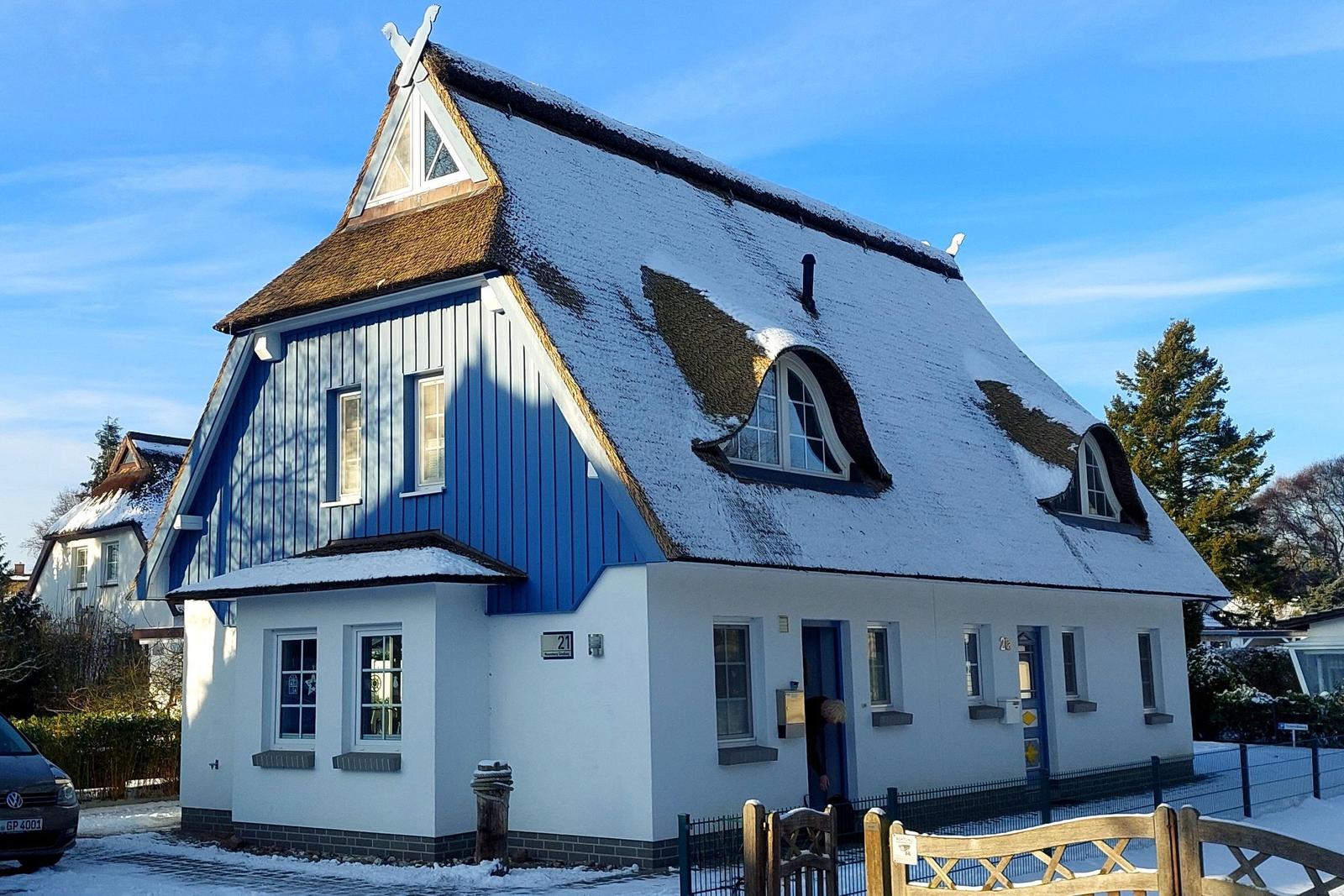 Ein Haus mit blauem Holz und weißem Putz, das Dach ist mit Schnee bedeckt.