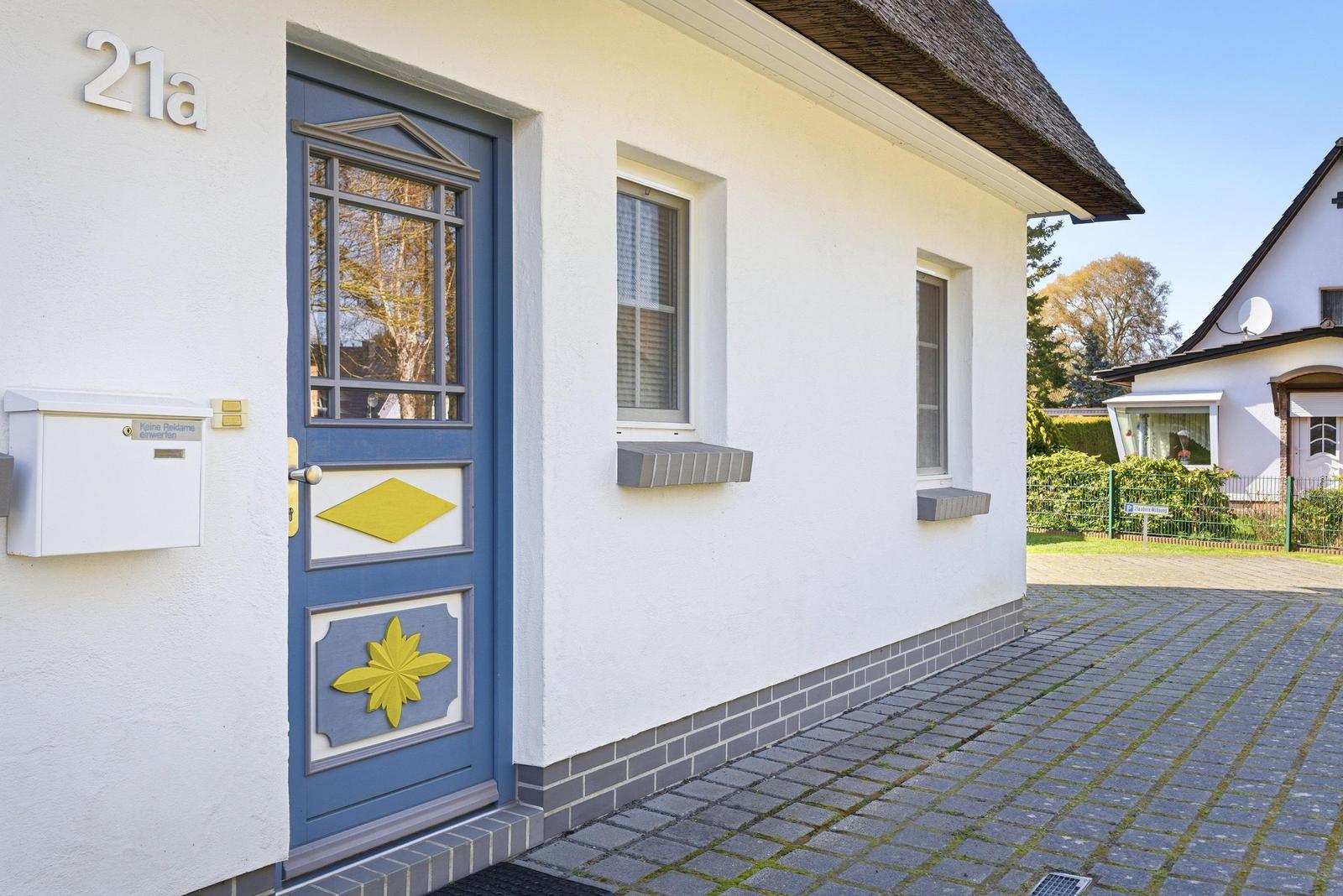 Haus mit blauer Tür und gelben Verzierungen, weiße Fassade und Steinplattenhof.