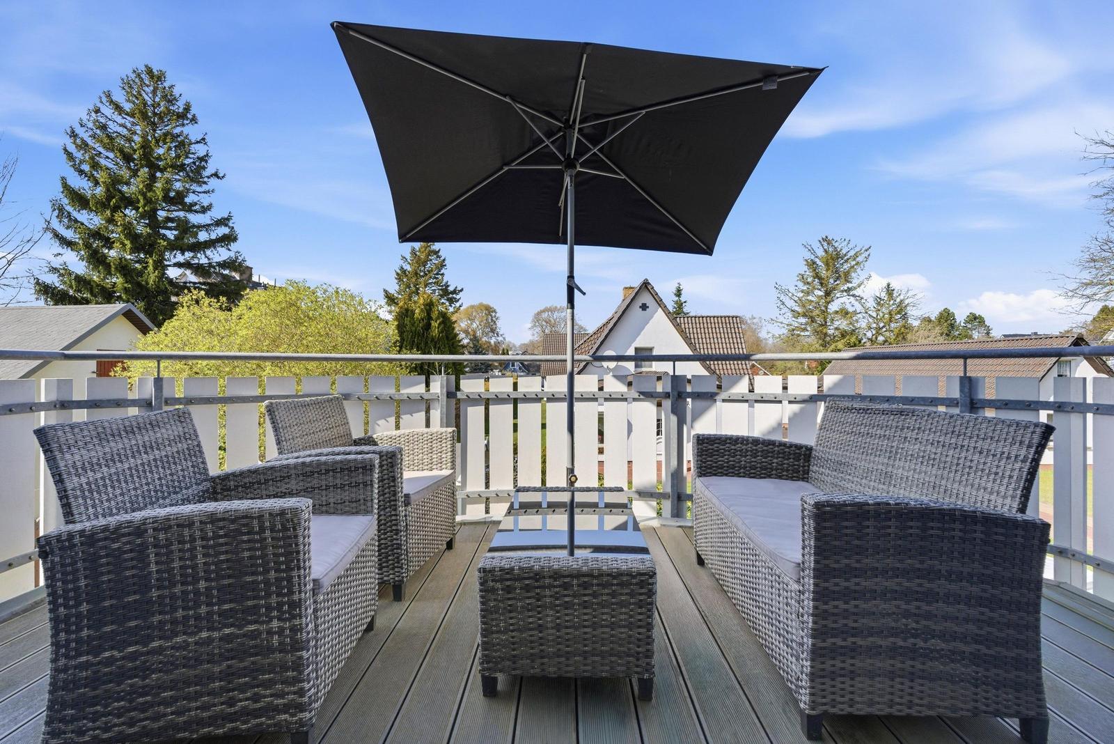 Terrasse mit Sitzgruppe, Sonnenschutz und Blick auf Wohnhäuser.