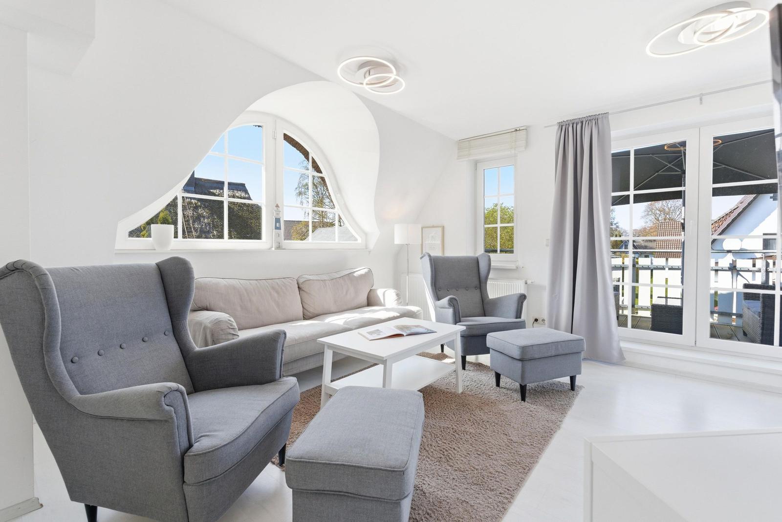 Wohnzimmer mit grauen Sesseln, Sofa und Glasfront zur Terrasse.