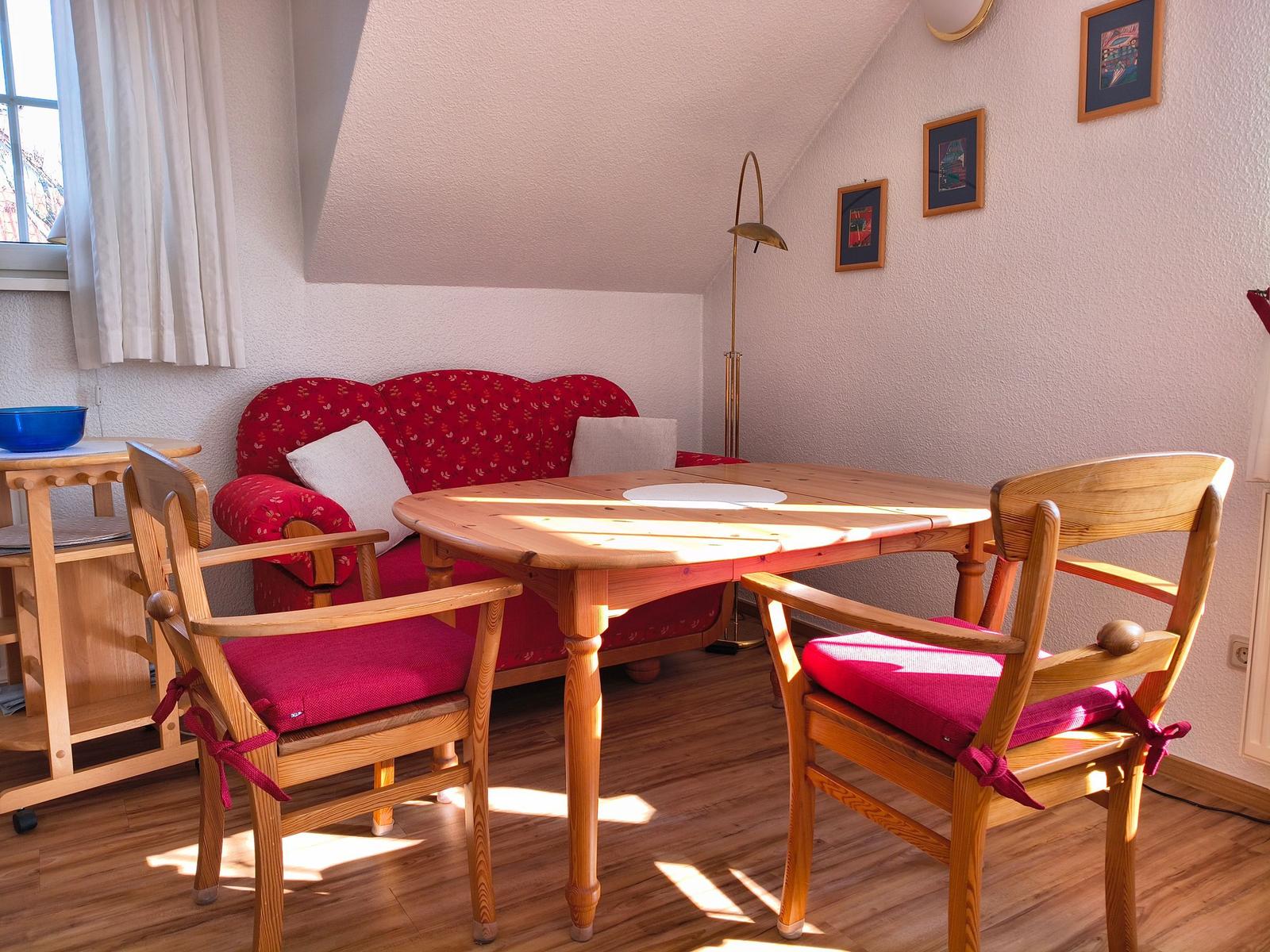 Ein Esszimmer mit Holztisch, zwei Stühlen und einem Sofa. An der Wand hängen Bilder.