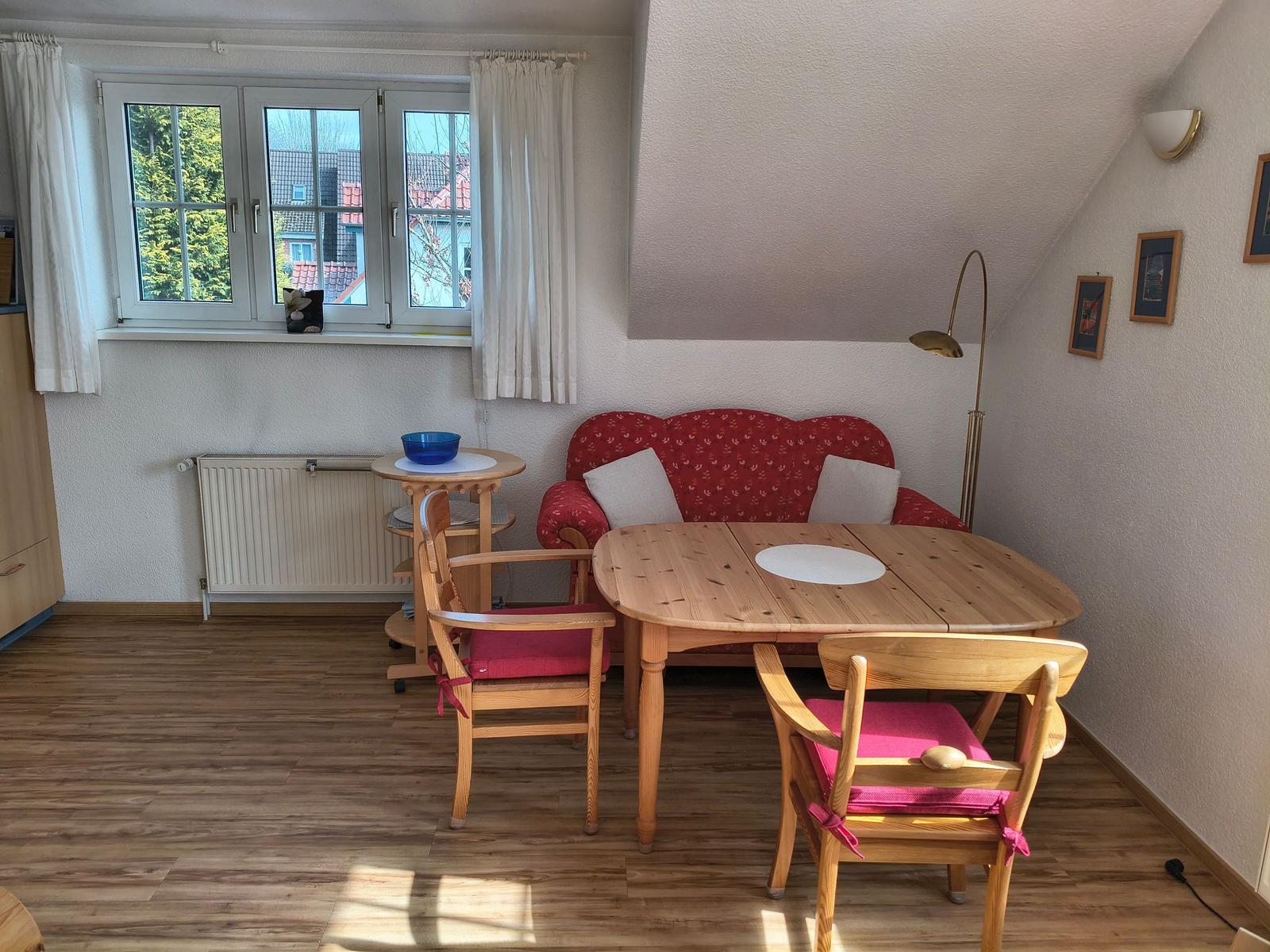 Ein Raum mit Holztisch, Stühlen, Sofa und Fenster mit Blick nach draußen.