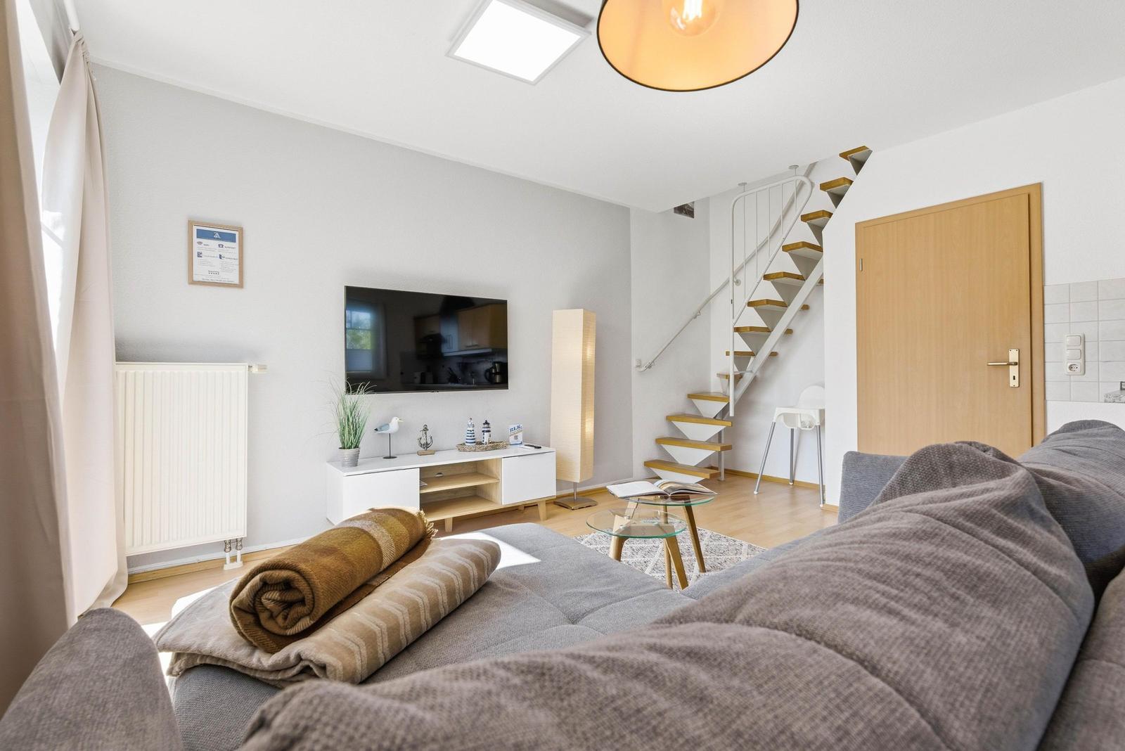 Wohnzimmer mit Sofa, Fernseher und Treppe zur oberen Etage.