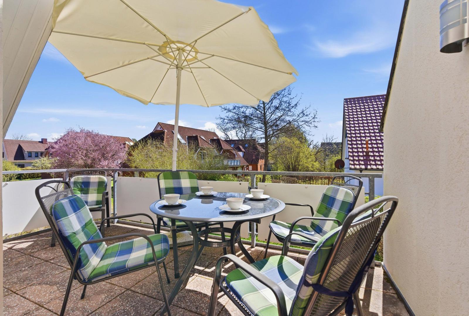 Terrasse mit Tisch, Stühlen und Sonnenschirm. Blick auf Wohnhäuser und Bäume.