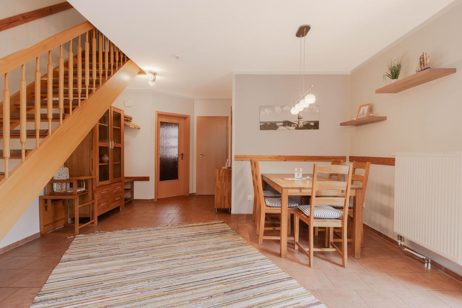 Eingangsbereich mit Essbereich, Holztreppe und Wohnbereich mit Teppich.