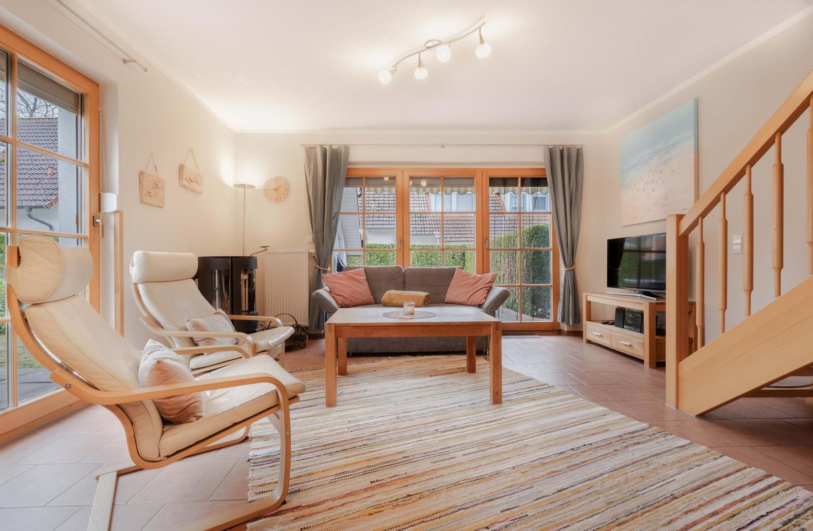 Wohnzimmer mit Sofa, zwei Sesseln, TV und Holztreppe.