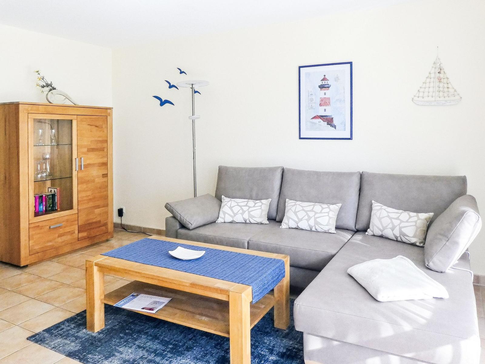 Ein Wohnzimmer mit grauem Sofa, Holztisch und Glasvitrine.