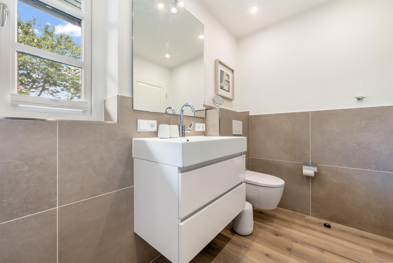 Badezimmer mit Waschbecken, Spiegel, Toilette und Fenster.