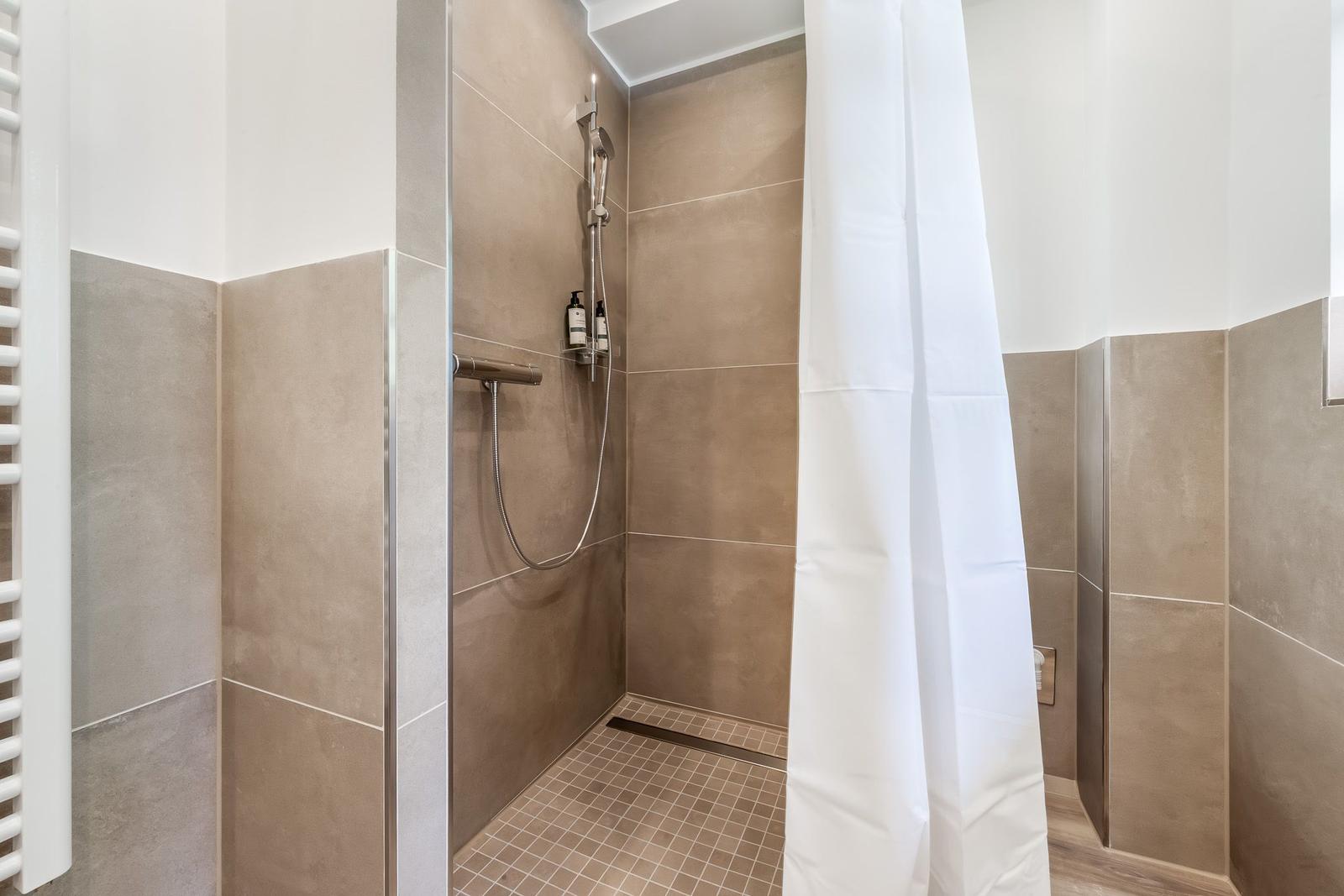 Dusche mit Duschbrause, Duschvorhang und Fliesen