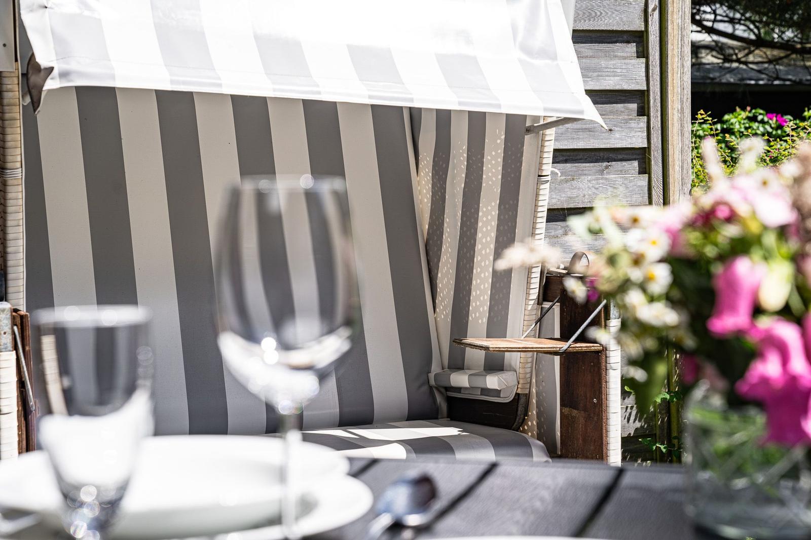 Terrasse mit gedecktem Tisch unter einem gestreiften Markisenüberdachung. Blumen und Gläser sind sichtbar.