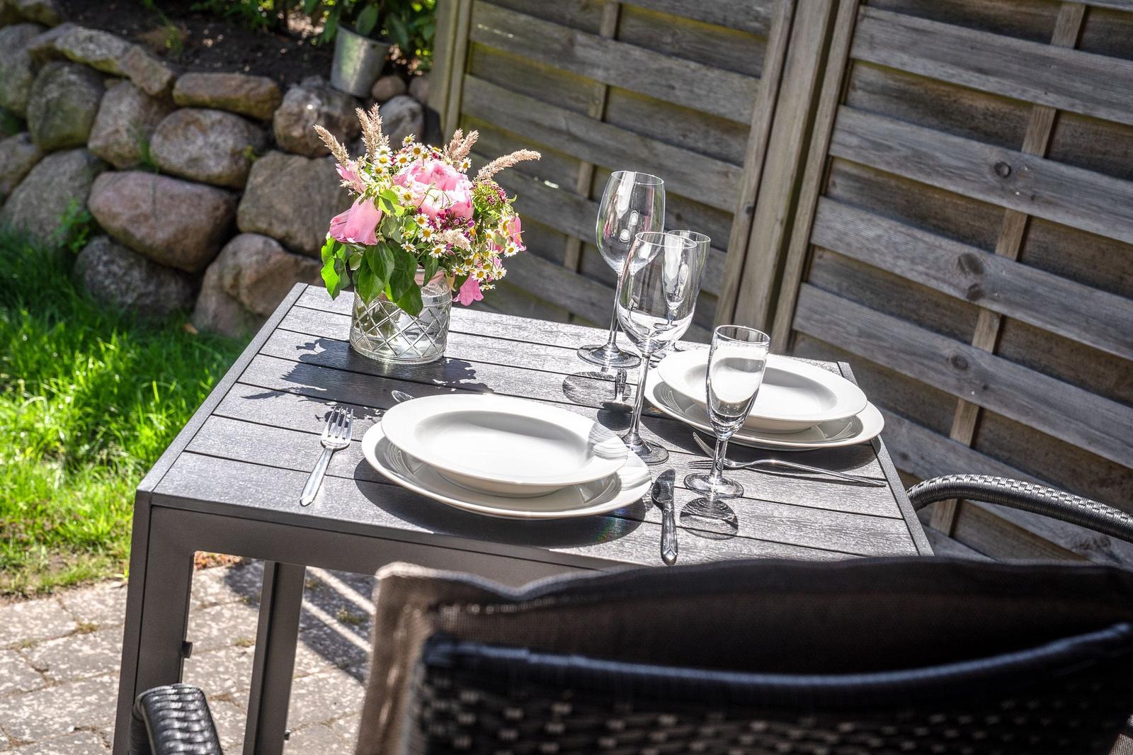 Garten-Tisch mit Platz für zwei, Blumen und Gläser.