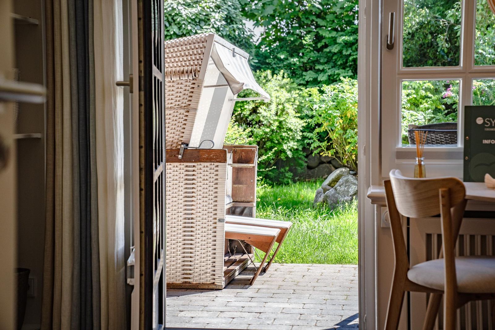 Durch die Tür ist ein Garten mit Liegestuhl und grüner Vegetation zu sehen.