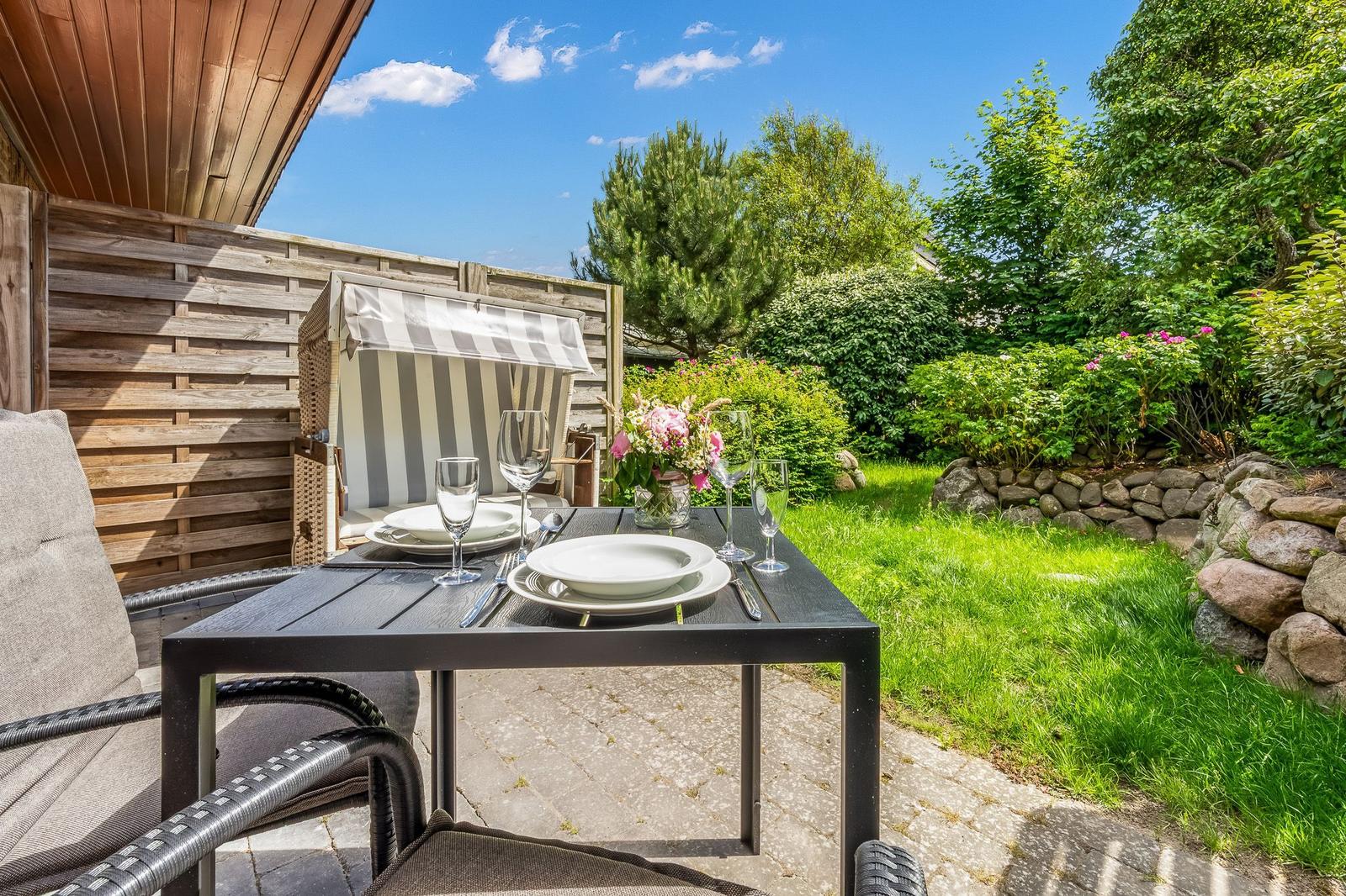 Garten mit Tisch, Stühlen und Sonnenschutz. Grünflächen und Steinmauer sind sichtbar.