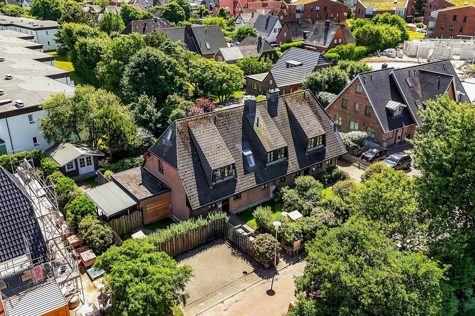 Haus mit Dachgauben und gepflastertem Hof, umgeben von Bäumen und Nachbarhäusern.