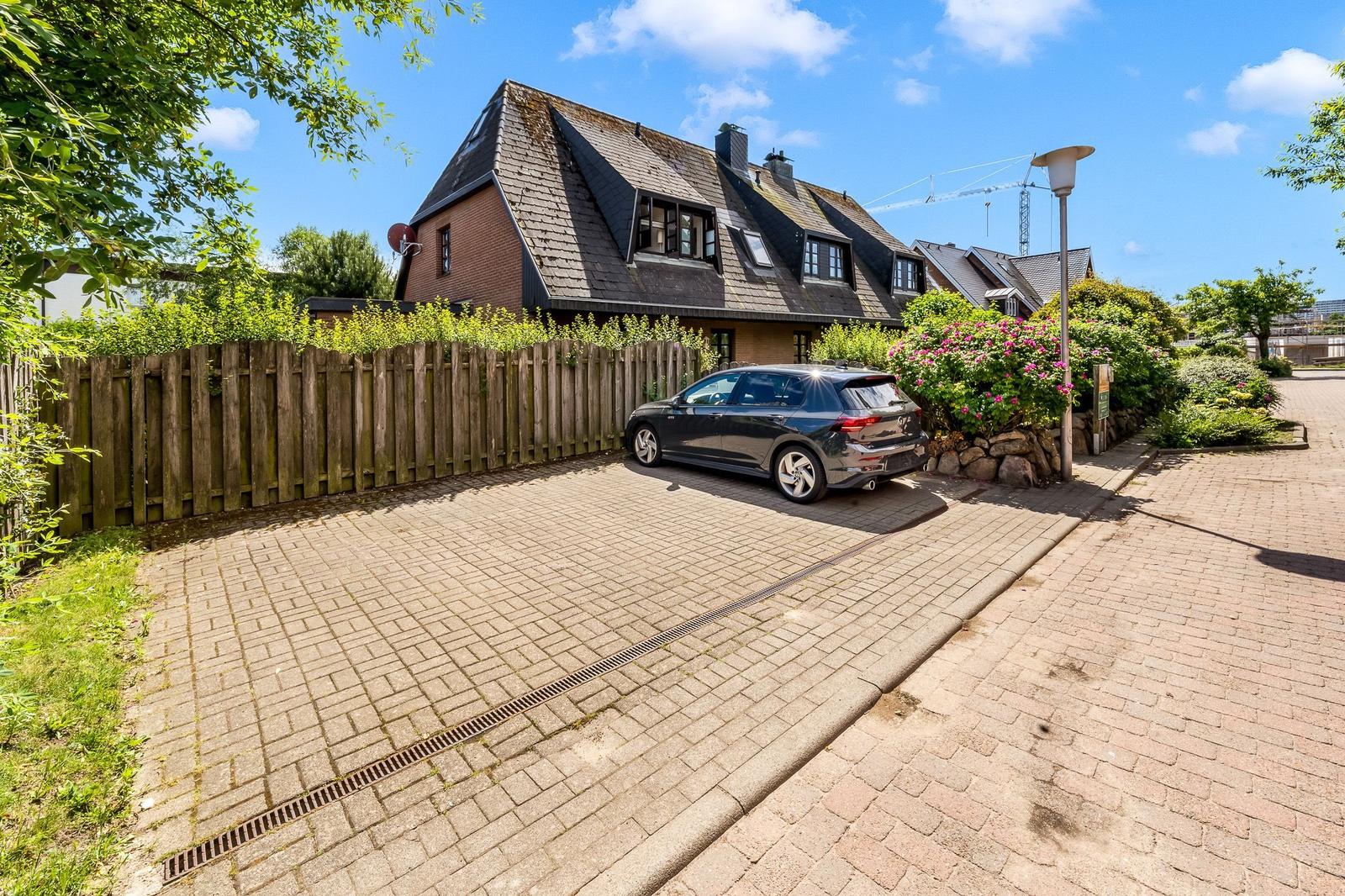 Haus mit Schieferdach, gepflasterter Hof und parkender Wagen.