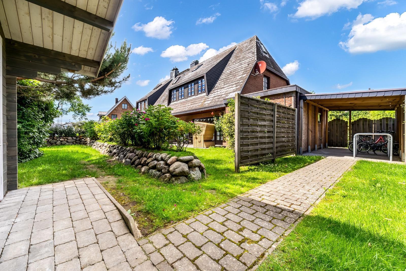 Haus mit Garten, Steinmauer, Pflanzen und Fahrradstellplatz unter Pavillon.