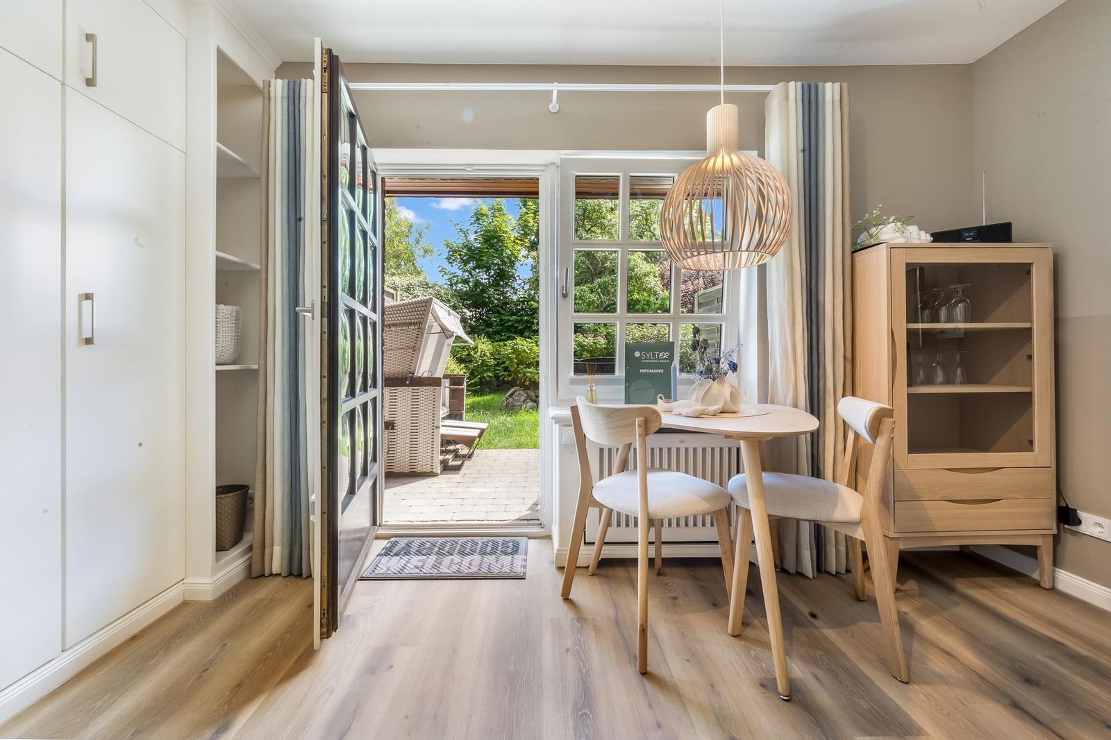 Essbereich mit Tisch, Stühlen und Glasvitrine. Tür führt auf Balkon mit Gartenblick.