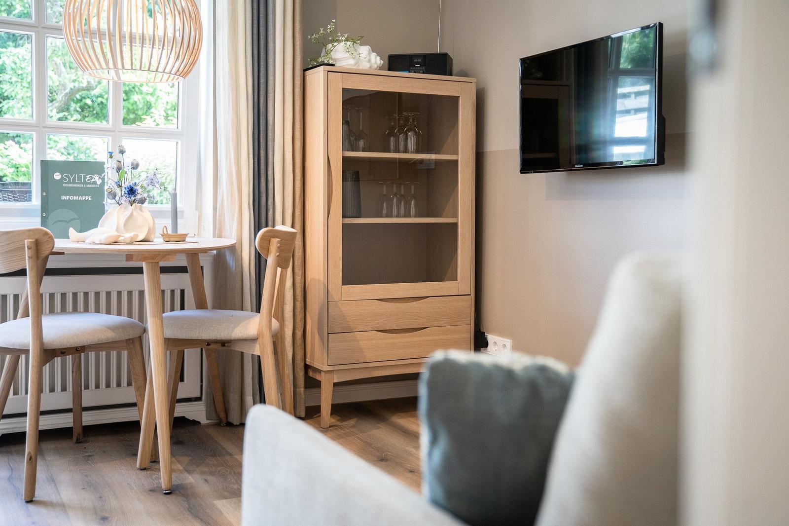 Esszimmer mit Tisch, Stühlen und Glasvitrine. Fernseher an der Wand.