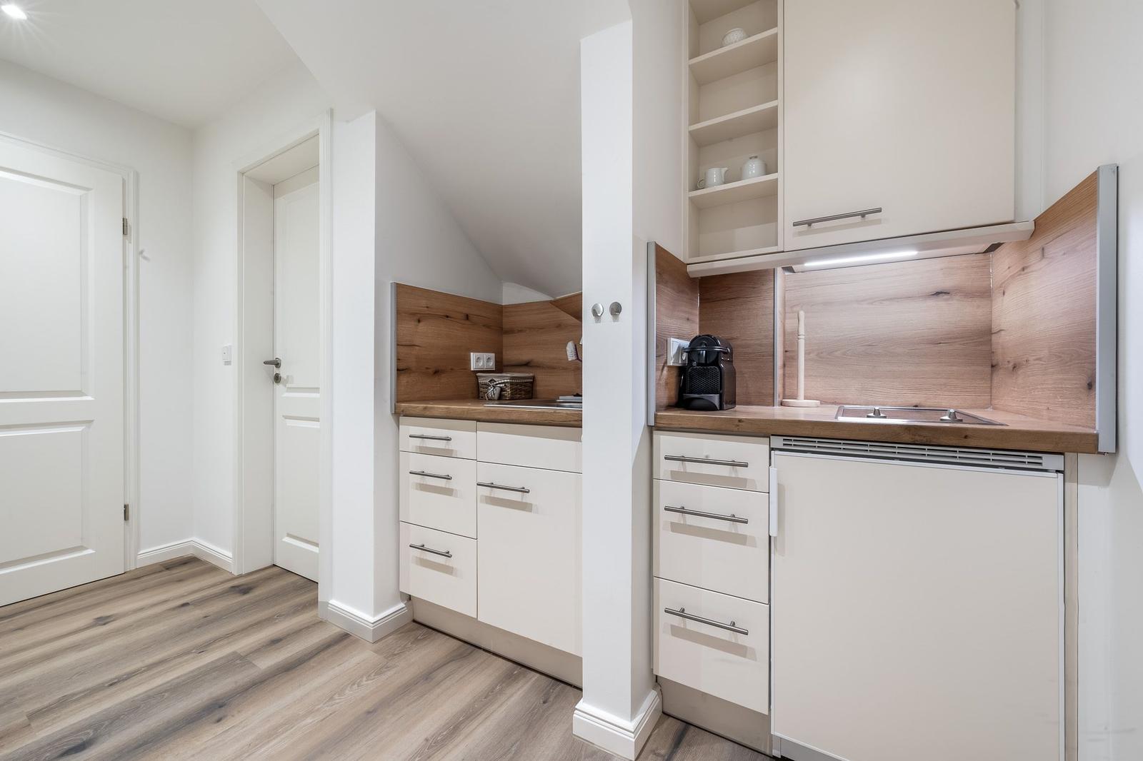 Küche mit weißen Schränken, Holzrückwand und integriertem Kühlschrank.