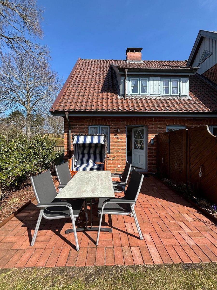 Haus mit Terrasse, Tisch, Stühlen und Liegestuhl. Roter Ziegelhof und Dach.