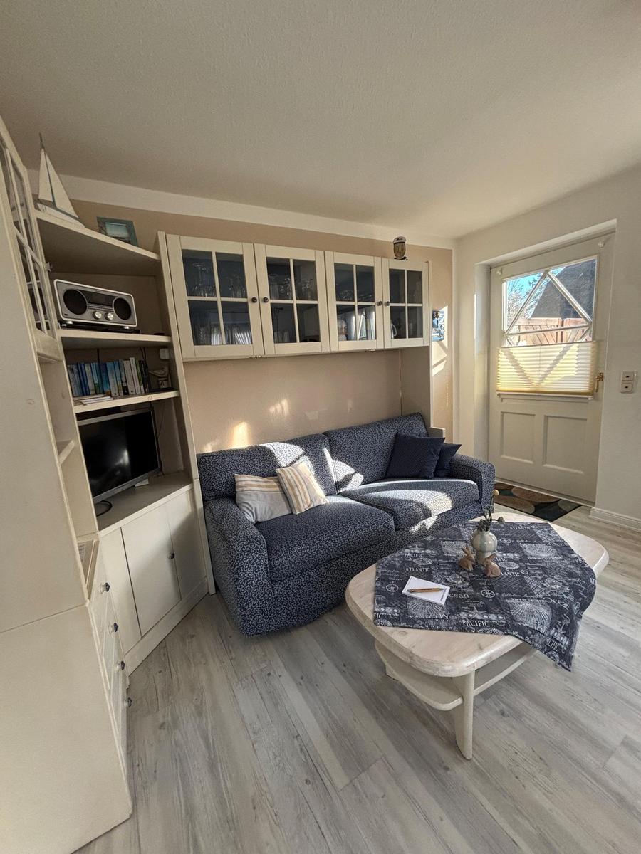 Wohnzimmer mit Sofa, Couchtisch und eingebautem Schrank. Fenster mit Jalousie.