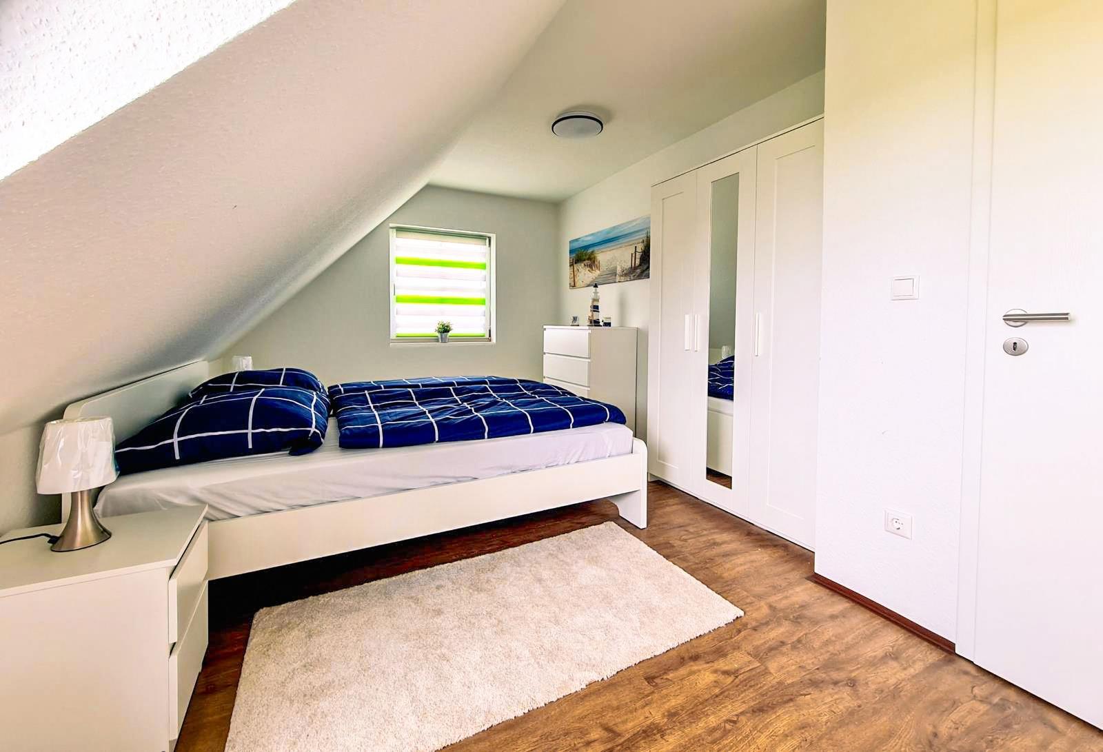 Schlafzimmer mit Dachschräge, Bett, Kleiderschrank und Fenster mit Jalousie.