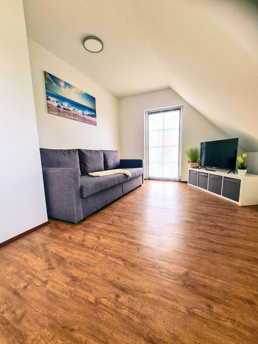 Wohnzimmer mit Sofa, TV und Holzboden unter schräger Decke.