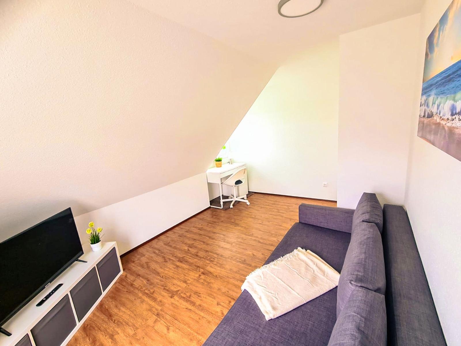 Wohnzimmer mit Sofa, Fernseher und Schreibtisch unter Dachschräge