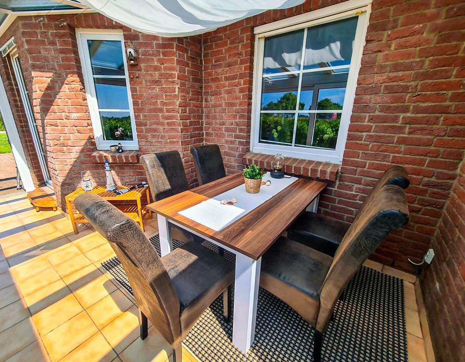 Terrassenbereich mit Esstisch, vier Stühlen und Fenstern an Backsteinmauer