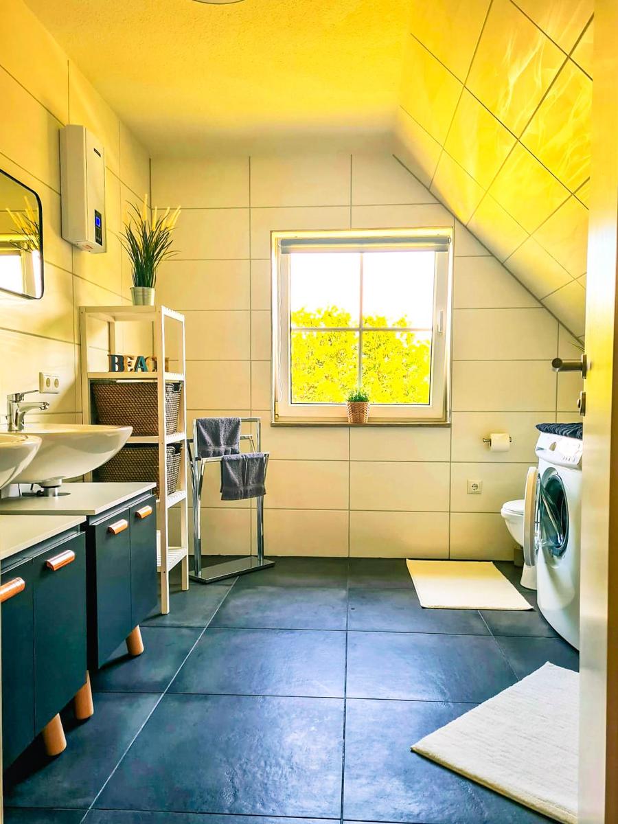 Badezimmer mit Waschmaschine, Fenster und hellen Fliesen.