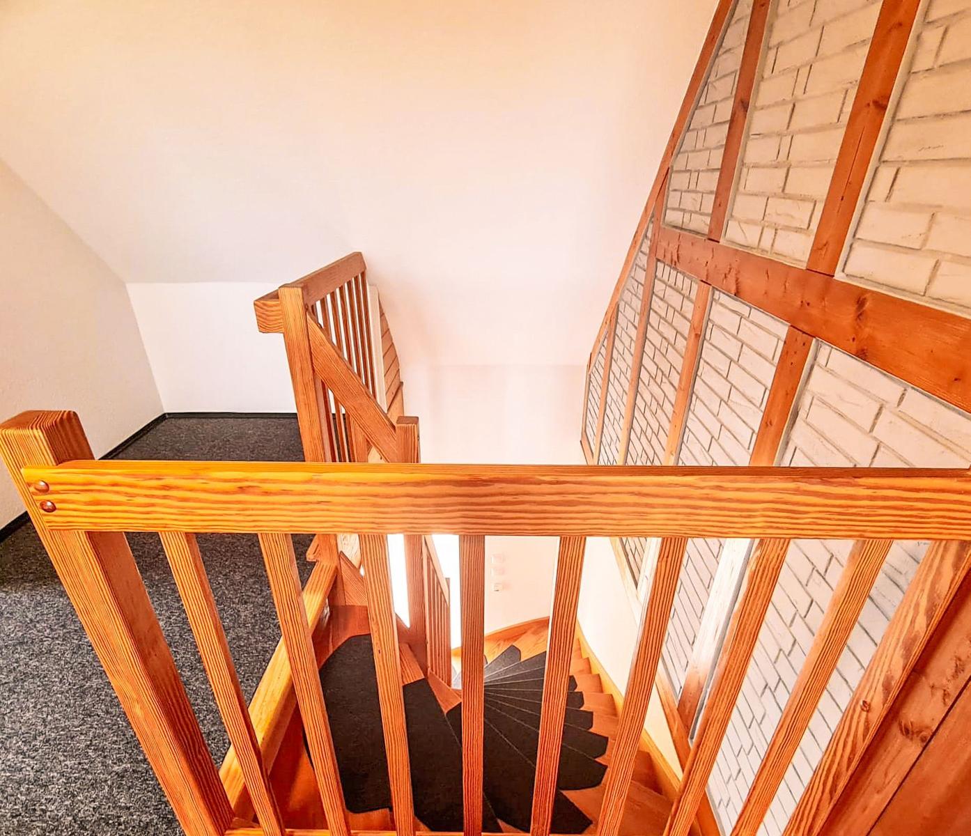 Holzgetreppe mit Geländer führt nach unten. Wand aus weißem Ziegel und Holzrahmen.