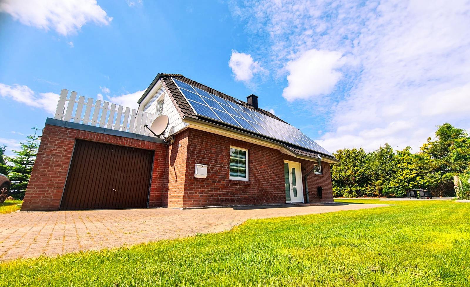 Ein Einfamilienhaus mit Solaranlage, Garage und grünem Garten unter blauem Himmel.