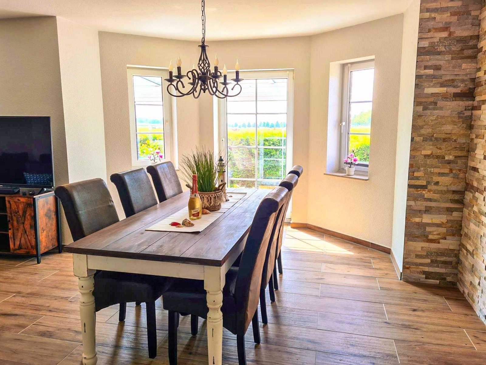 Esszimmer mit Holztisch, Stühlen und Fensterblick auf Grünflächen.