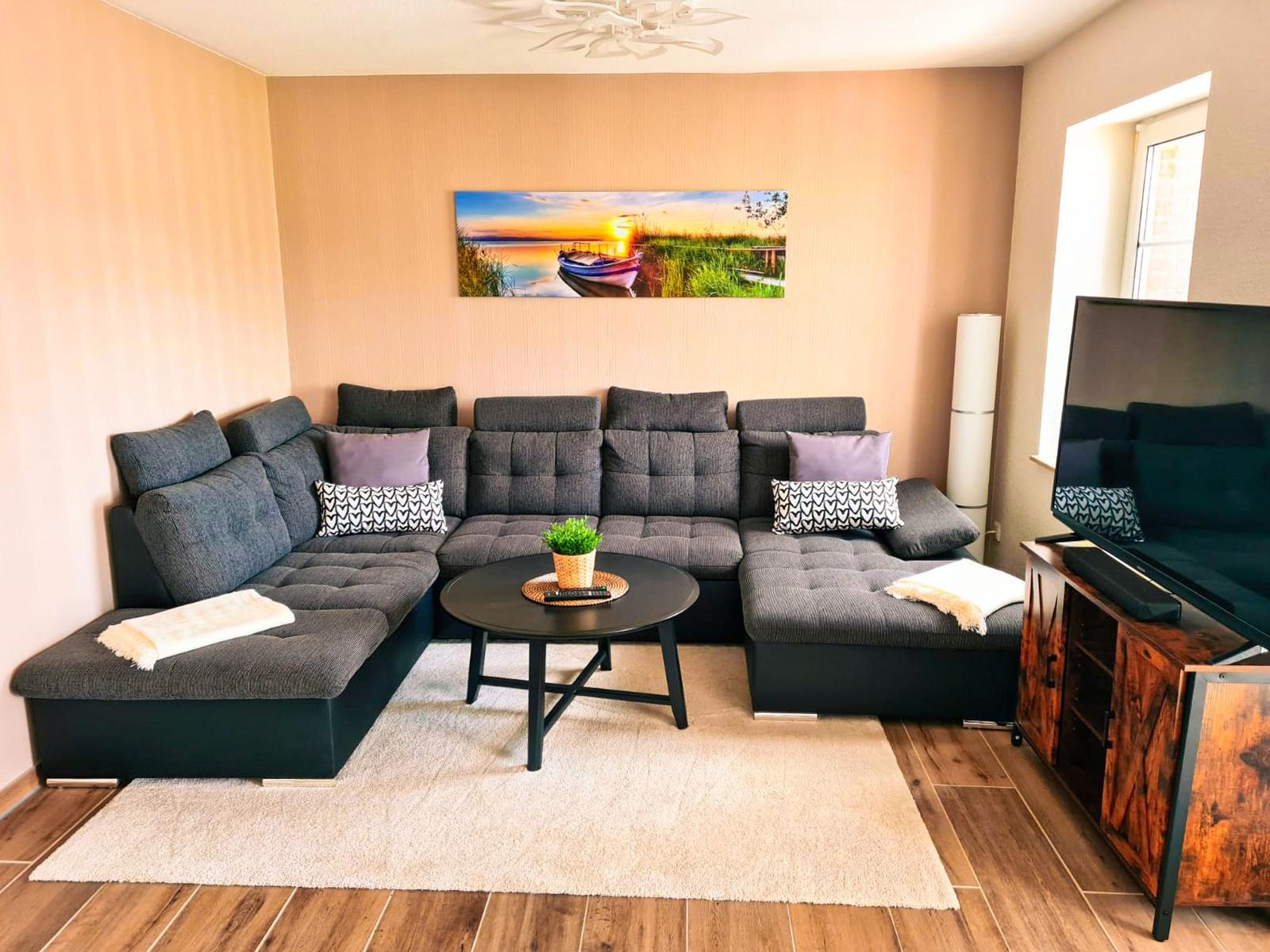 Ein Wohnzimmer mit einem großen grauen Sofa, einem runden Tisch und einer Wanddekoration.
