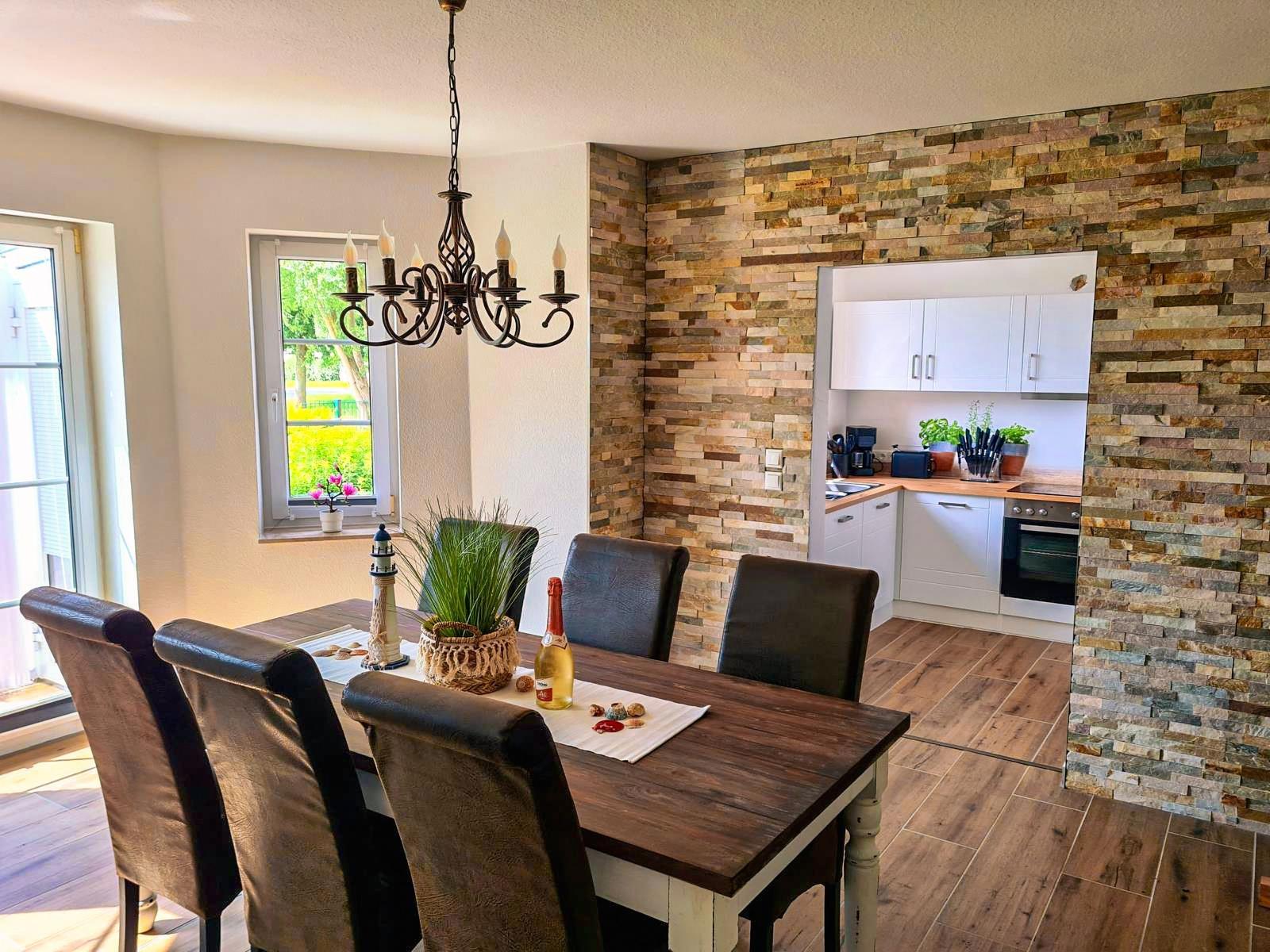 Essbereich mit Tisch, Stühlen und Küchenbereich mit Steinwand