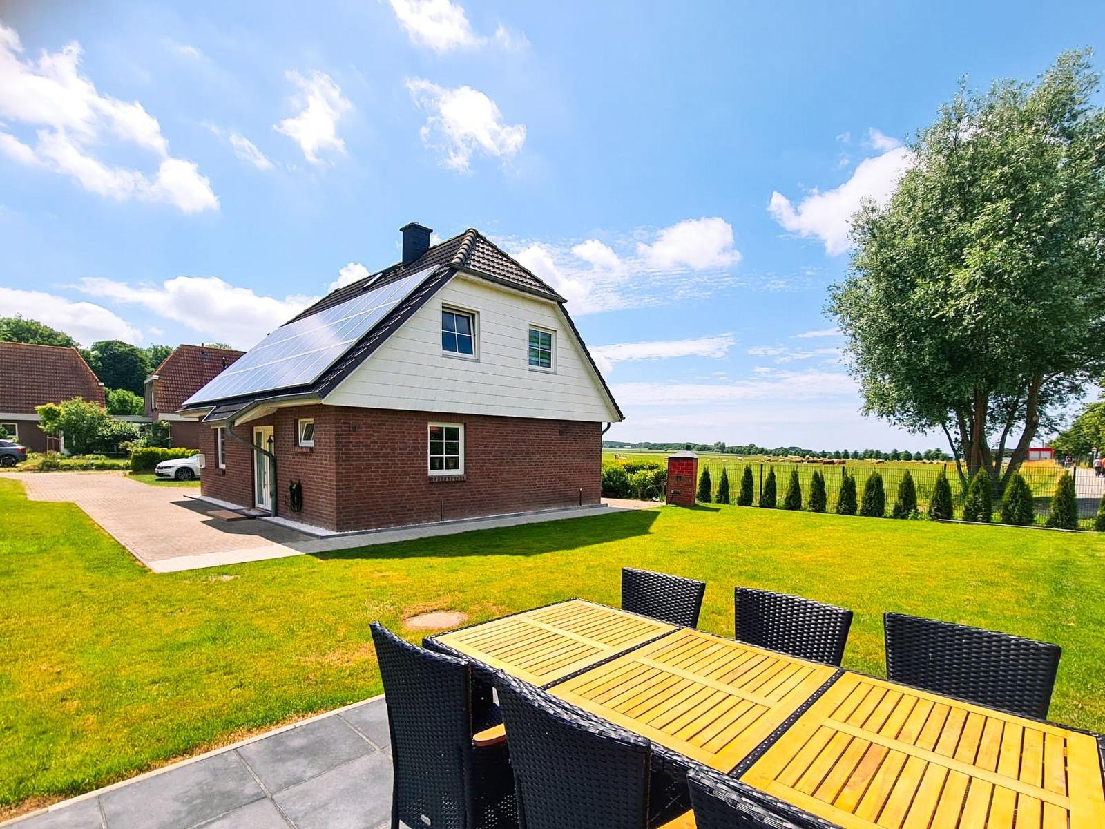 Haus mit Solaranlage, großer Garten und Terrasse mit Tisch und Stühlen.