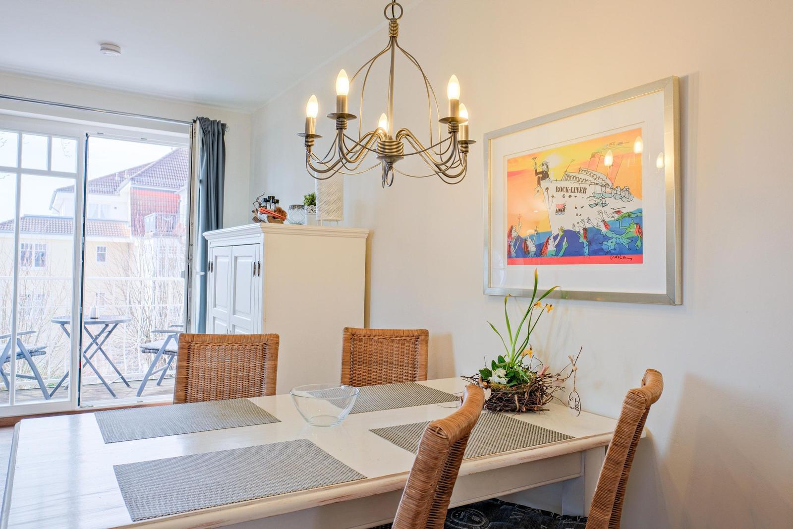 Esstisch mit vier Stühlen, Kronleuchter und Wandbild. Durchgang zur Terrasse.